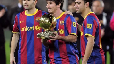 Lionel Messi sostiene el Balón de Oro junto a Andrés Iniesta y Xavi Hernández con la camiseta del Barcelona.