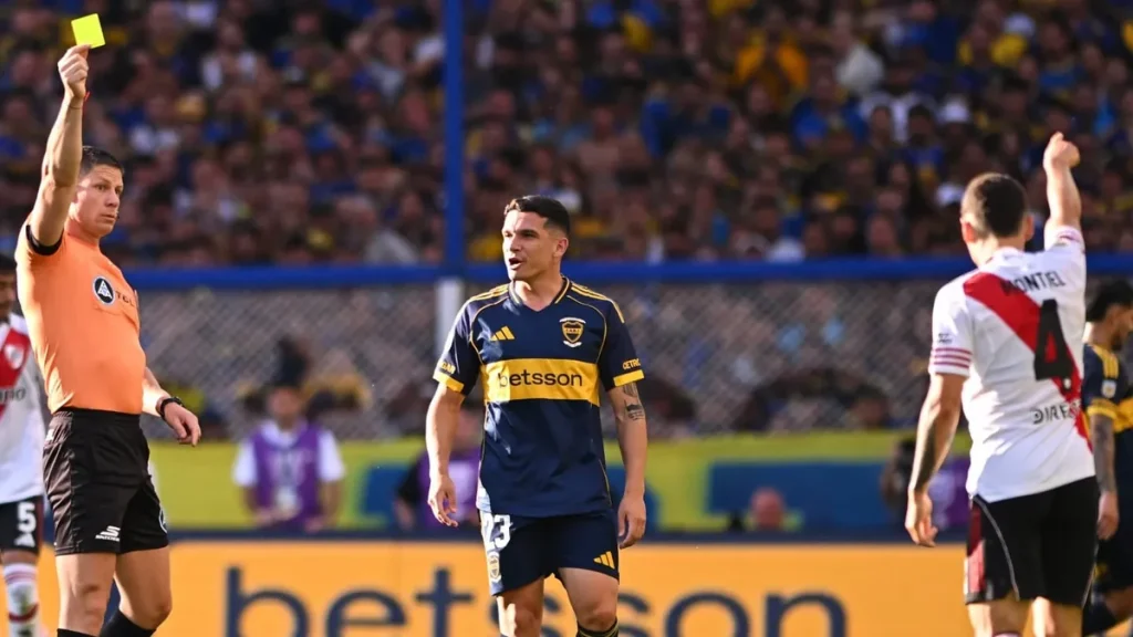 Nicolás Ramírez levanta una tarjeta amarilla durante un Superclásico entre Boca y River.