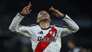 Un jugador de River con la camiseta blanca y banda roja levanta los brazos.