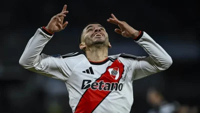 Un jugador de River con la camiseta blanca y banda roja levanta los brazos.